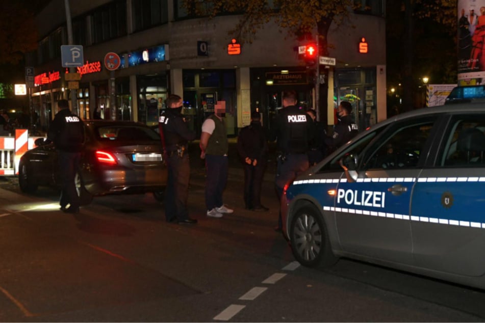 Einer der mutmaßlichen Dealer wurde von den Polizeibeamten festgenommen und steht auf der Straße. Im Hintergrund steht der Mietwagen.