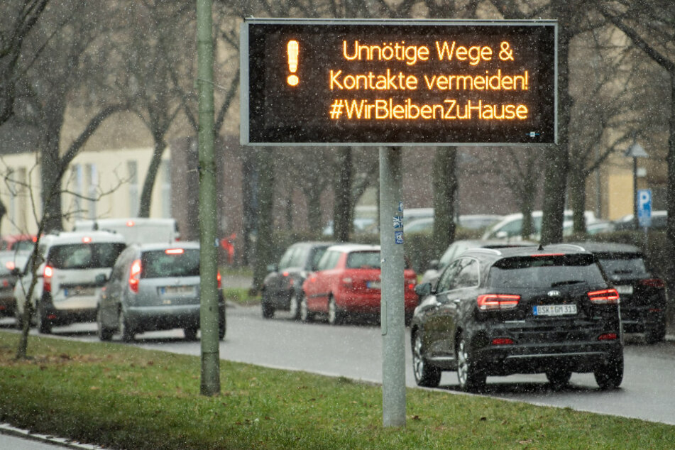 Autos fahren an einem großen Display mit Hinweisen zur Corona-Pandemie am Tempelhofer Damm vorbei, hier heißt es: Unnötige Wege &amp; Kontakte vermeiden! #WirBleibenZuHause
