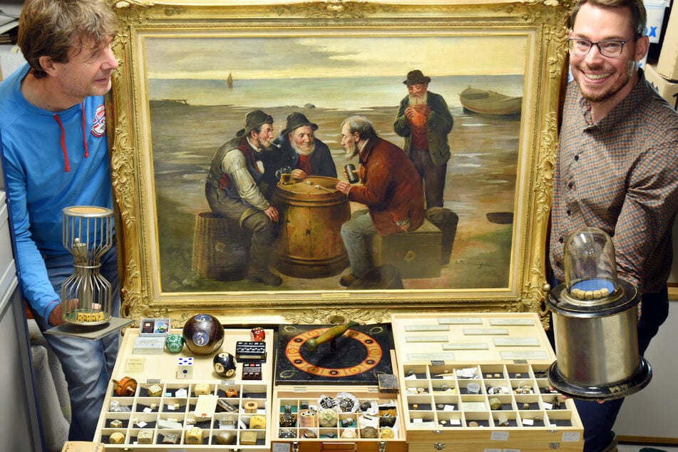 Der Würfelspielesammler Jakob Gloger (34, r.) steht mit seinem Vater André (59) in seiner Würfelspielesammlung, zu der neben vielen Tausenden Würfel auch ein großes Gemälde gehört, das Fischer beim Würfeln auf einem Heringsfass um 1910 zeigt.