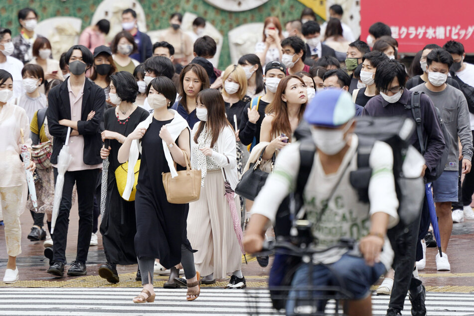 Passanten mit Mundschutzen gehen auf einer stark frequentierten Straße vor dem Bahnhof JR im Stadtteil Shibuya.