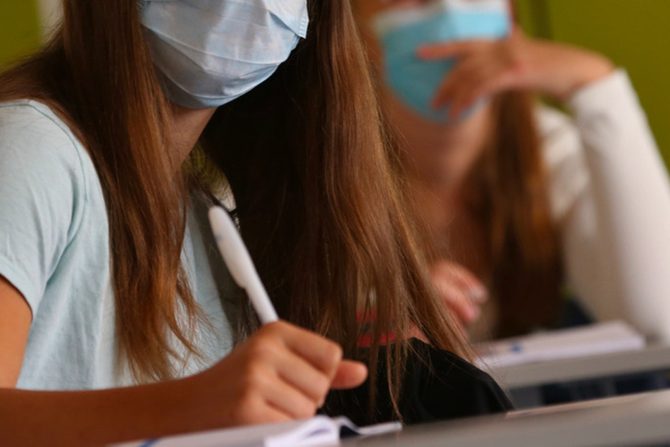 Schülerinnen einer neunten Klasse einer Mittelschule sitzen am ersten Schultag zu Beginn des Unterrichts mit Mundschutz im Klassenzimmer.