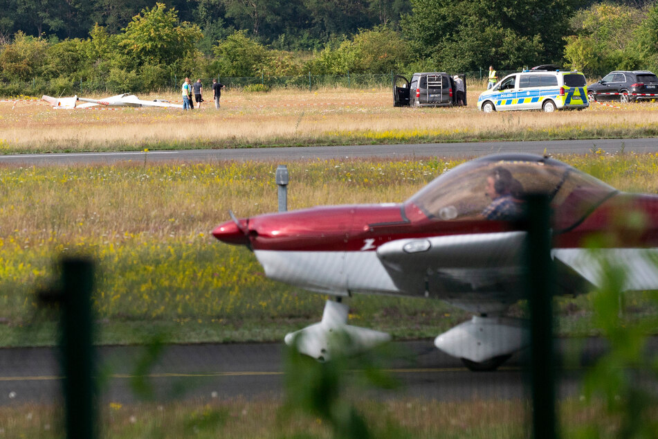 Ein abgestürztes Segelflugzeug liegt auf dem Flugplatz Hangelar bei Bonn, während im Vordergrund ein Sportflugzeug vorbeirollt.