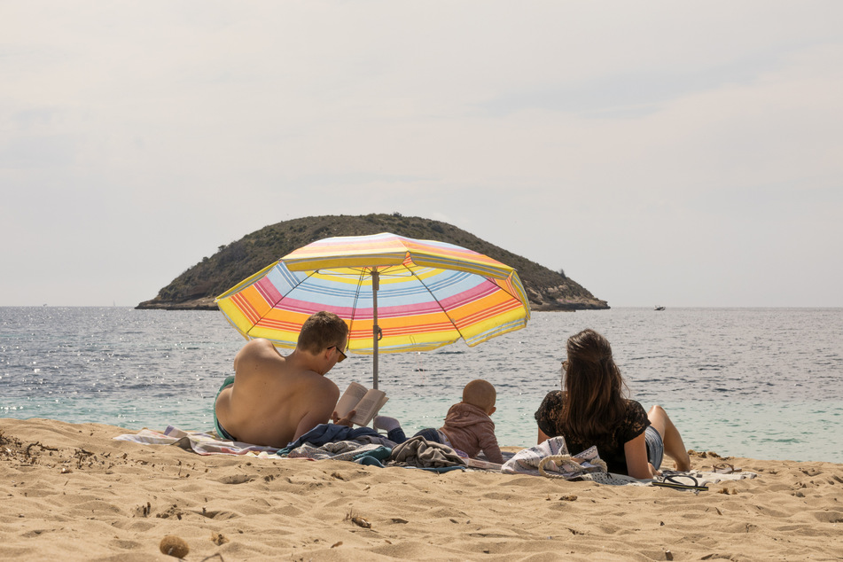 Spanien, Magaluf: Eine Familie liegt unter einem Sonnenschirm am fast leeren Strand von Magaluf auf Mallorca. Der große Ansturm auf die Insel blieb trotz Lockdown-Ende aus.