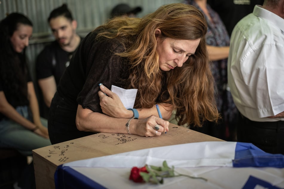 Ricarda Louk schreibt während der Beerdigung auf den mit einer Flagge bedeckten Sarg ihrer Tochter Shani Louk (†22).