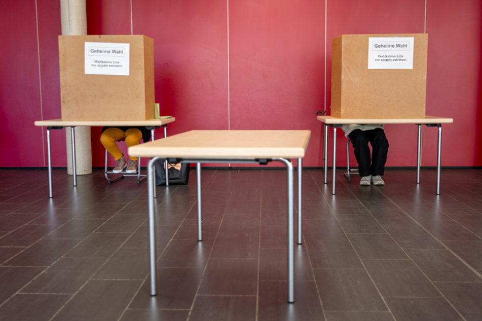 Hinter einem Sichtschutz nehmen Wähler in einer zum Wahllokal umfunktionierten Schule an der bayerischen Kommunalwahl teil.