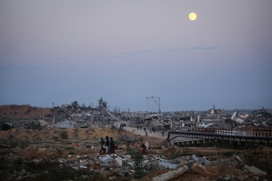 People walk amid the rubble of destroyed buildings as the Cold Moon, the last supermoon of the year, rises over the Nuseirat camp for displaced Palestinians in the central Gaza Strip on December 4, 2025.