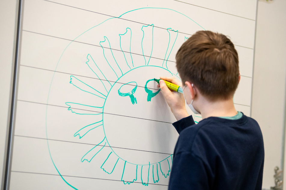 Ein Schüler einer vierten Klasse einer Grundschule zeichnet ein Corona-Virus an die Tafel.