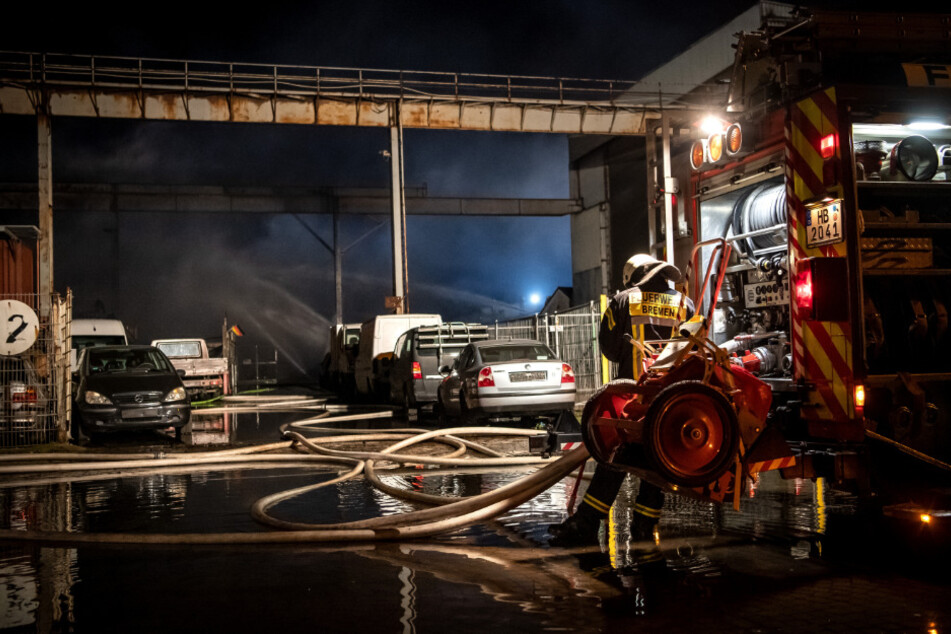 Feuerwehrleute stehen vor einer Lagerhalle, in der es nach einer Explosion zu einem Großbrand kam.