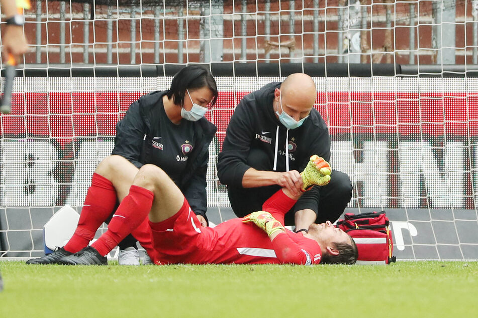 Martin Männel liegt auf dem Rasen und von Teamarzt Stephan Rezmann (r.) sowie Physiotherapeutin Marie Koch behandelt.