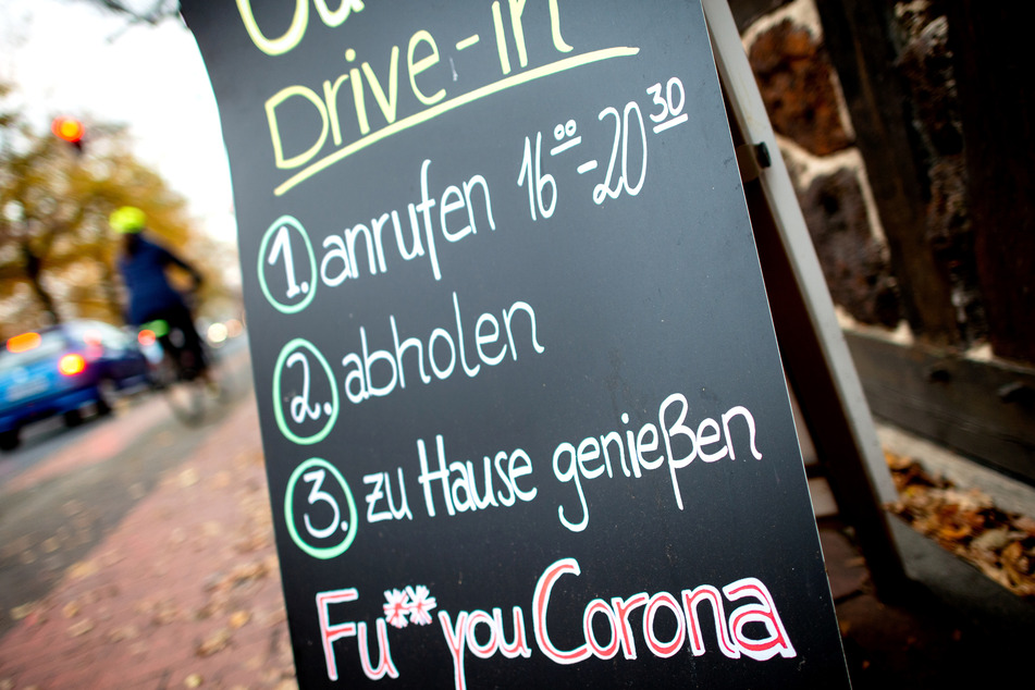 Eine Tafel mit der Aufschrift "Drive-in" und der Botschaft "Fu** you Corona" steht vor einem geschlossenen Restaurant.