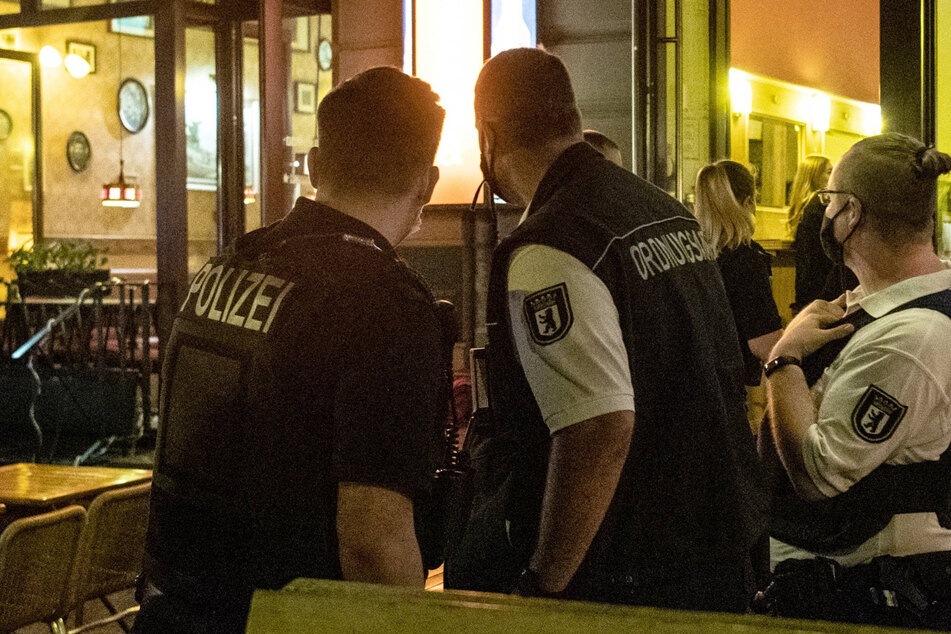 Ein Polizeibeamter und zwei Mitarbeiter des Ordnungsamtes stehen vor einem Lokal in Berlin.