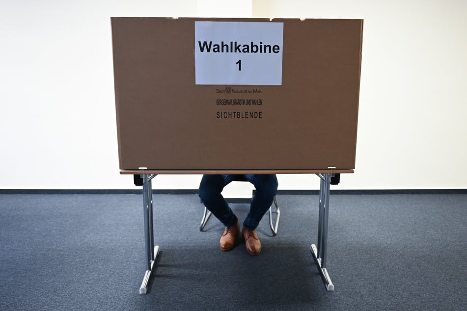 Ein Mann sitzt im Wahlraum des Briefwahllokals Frankfurt Innenstadt hinter einer Wahlkabine.