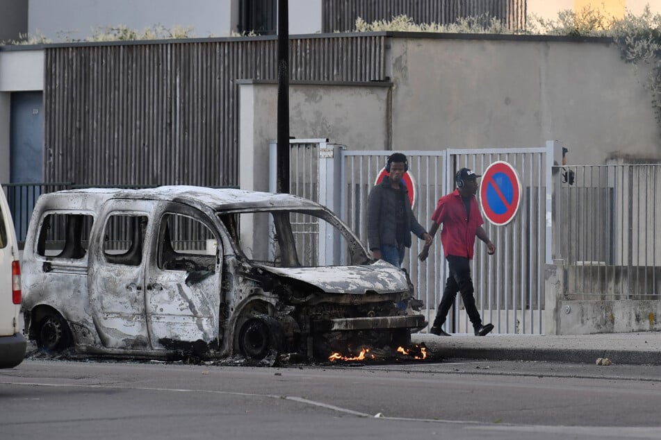 Menschen laufen nach Krawallen im Vorort Gresilles an einem abgebrannten Lieferwagen vorbei.