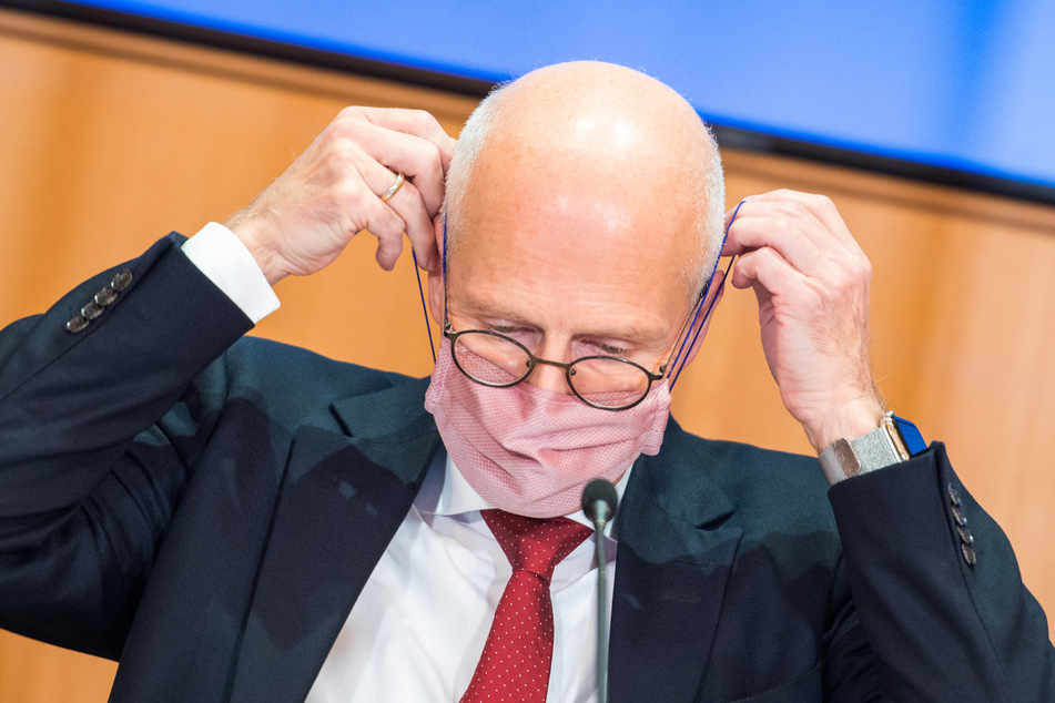 Peter Tschentscher (SPD) setzt sich im Rathaus während einer Pressekonferenz seine Maske (Mund-Nasen-Bedeckung) auf.