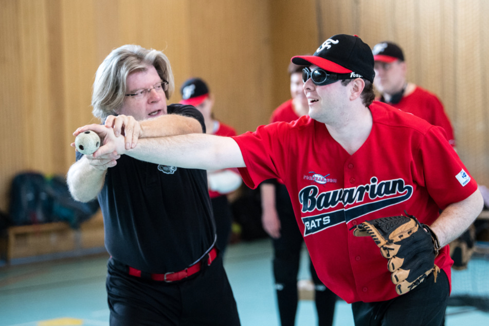 Hubertus Hagemeyer, Trainer (l), hilft Tobias Geitner, Spieler der Blindenbaseball-Mannschaft "Bavarian Bats", während einer Trainingseinheit bei der Wurftechnik.