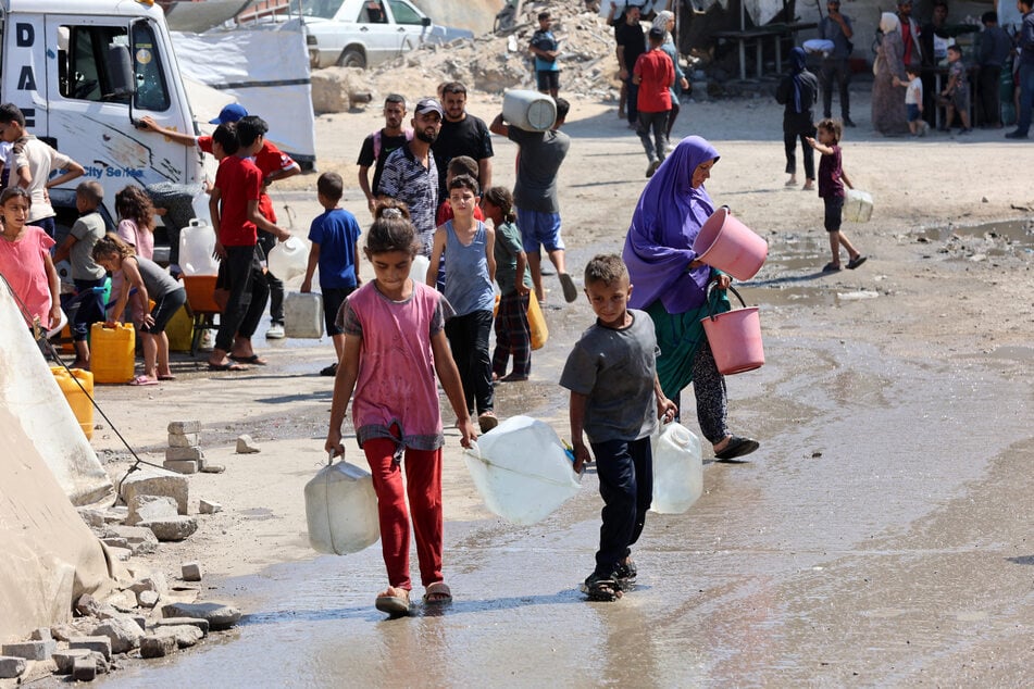 Palestinian children carry gallons of clean water from a distribution point in Gaza City on August 1, 2025.