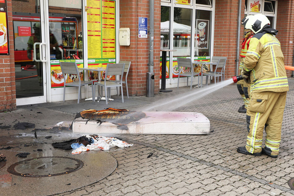Zigarette trifft Matratze: Feuerwehrleute löschen den Brandherd vor dem Haus.