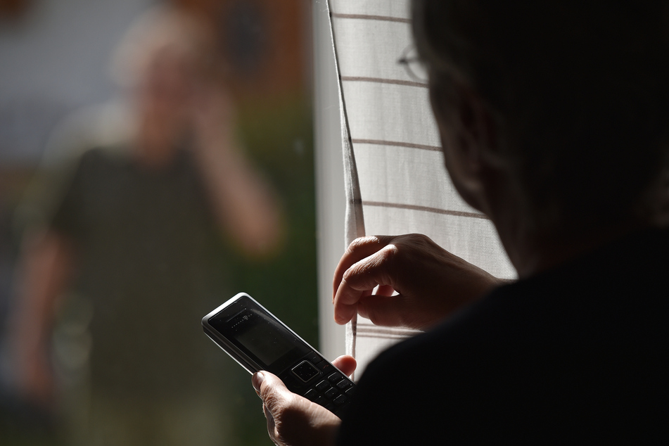 Eine Frau steht mit einem Telefon am Fenster, vor dem ein Mann steht. (Symbolbild)