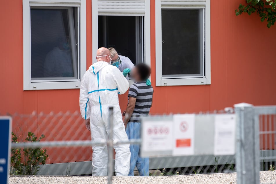 Eine Person im Schutzanzug nimmt an einer Wohncontaineranlage für Flüchtlinge einen Abstrich bei einem Bewohner der Anlage.