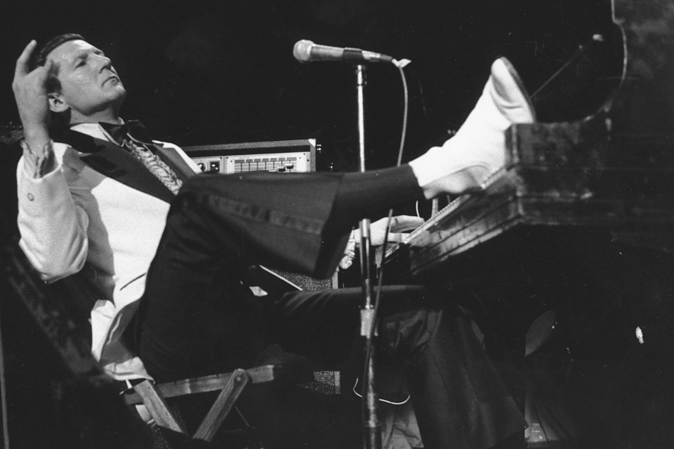1975: Jerry Lee Lewis stützt seinen Fuß auf ein Klavier, während er sich zurücklehnt und den Applaus der Fans während des fünften jährlichen Rock 'n' Roll Revival im New Yorker Madison Square Garden entgegennimmt.