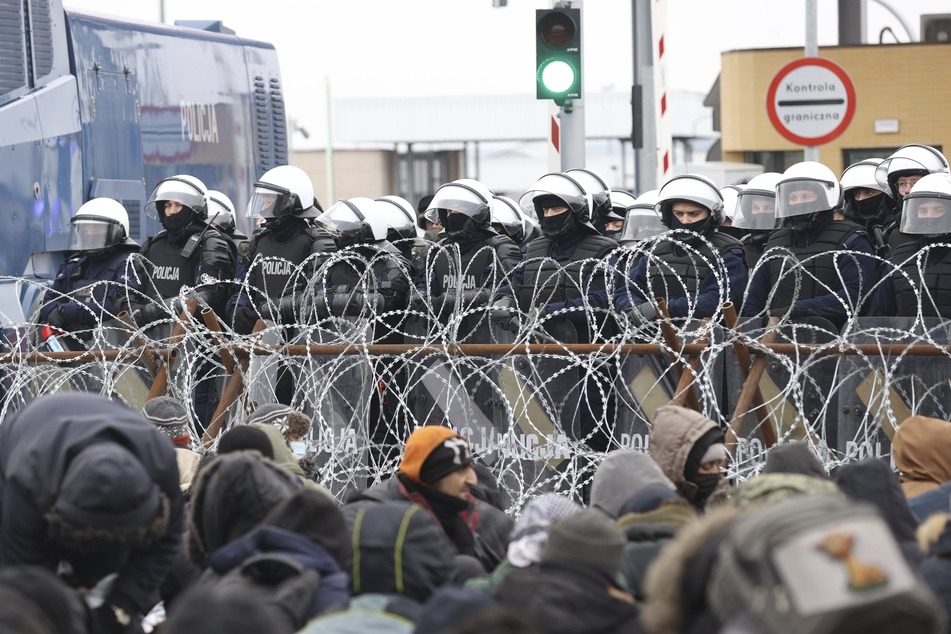 Hier stehen Migranten, die sich vor einem Stacheldrahtzaun am Kontrollpunkt Kuznica an der belarussisch-polnischen Grenze versammelt haben, der Polizei hinter Stacheldraht gegenüber.