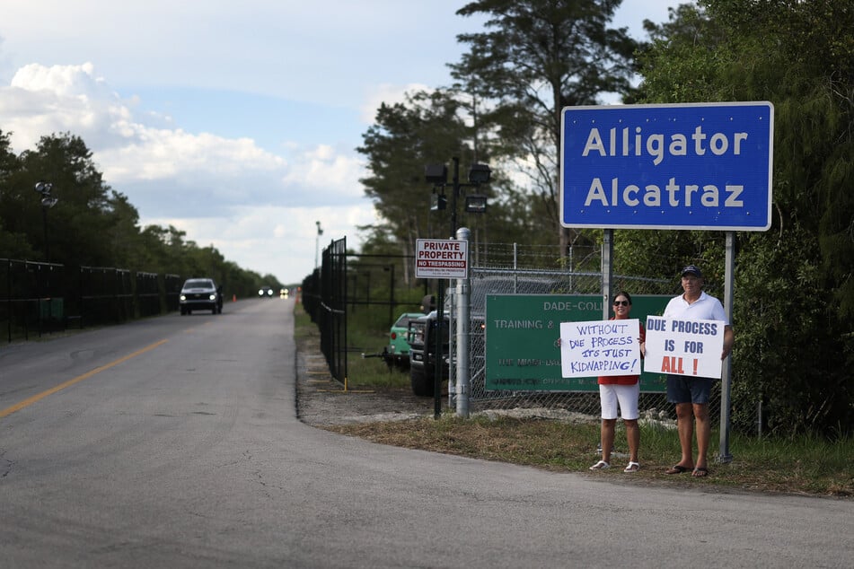 Protesters hold signs near the entrance to the state-managed immigration detention center dubbed Alligator Alcatraz, located at the Dade-Collier Training and Transition Airport in the Florida Everglades.