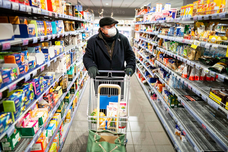 Ein Kunde kauft mit Mundschutz und Handschuhen am frühen Morgen in einem Supermarkt ein.