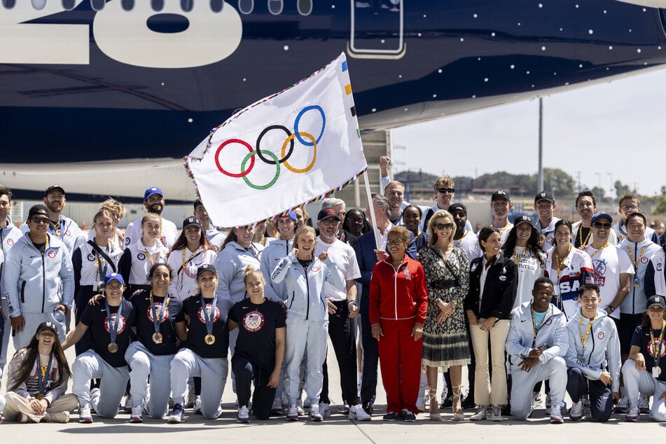 Olympic athletes and officials pose alongside Los Angeles Mayor Karen Bass, LA28 chairman Casey Wasserman, and California Governor Gavin Newsom, waving the Olympic flag during the event celebrating the arrival of the Olympic flag at Los Angeles International Airport (LAX) in Los Angeles, on August 12, 2024.