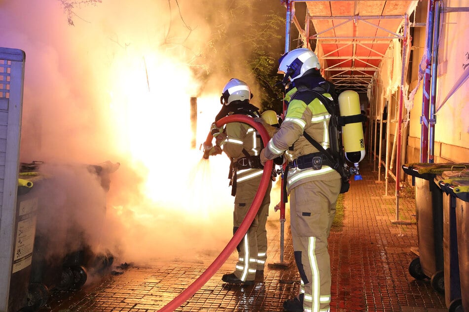 Einsatzkräfte unter Atemschutz löschen mit einem Strahlrohr den Brand eines Müllbehälters. (Symbolfoto)