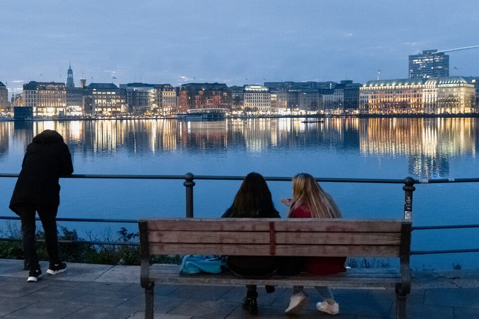 Menschen sitzen und stehen bei milden Temperaturen in der Abenddämmerung an der Binnenalster in Hamburg.