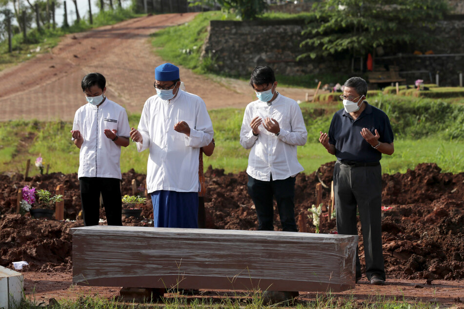 Ein islamischer Geistlicher betet mit Angehörigen bei der Beerdigung eines Mannes in dem Abschnitt eines indonesischen Friedhofs, der für Corona-Verstorbene bestimmt ist.