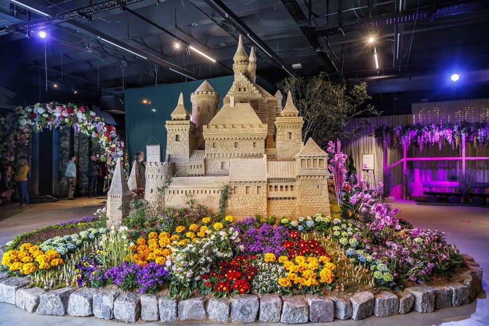 Eine filigrane Sandburg erstrahlt in bunter Blumenvielfalt.