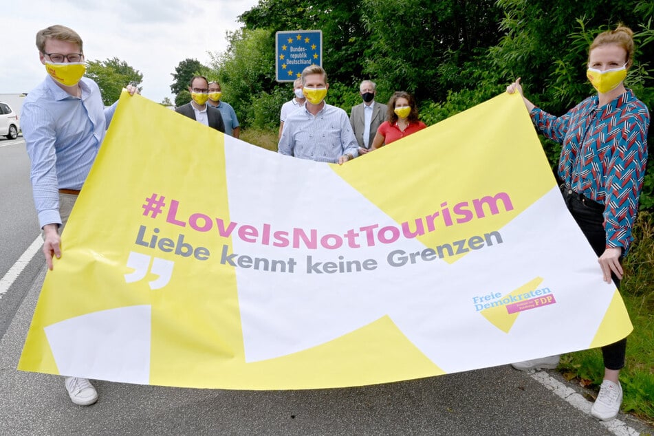 Mit einer Schutzmaske steht Heiner Garg (M.), FDP-Landesvorsitzender und Gesundheitsminister von Schleswig-Holstein, bei einer Demonstration am Grenzübergang Padborg. Links steht Moritz Körner, FDP Eurpaabgeordneter, rechts Gyde Jensen, Bundestagsabgeordnete. Die Politiker fordern, dass unverheiratete Lebenspartner aus Nicht-EU-Staaten nach Deutschland einreisen dürfen.