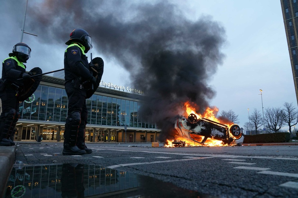 Flammen schlagen aus einem Auto, das vor dem Bahnhof in Eindhofen auf dem Kopf liegt. Mehrere hundert Menschen haben dort am Sonntag gegen die aktuelle Corona-Politik demonstriert.