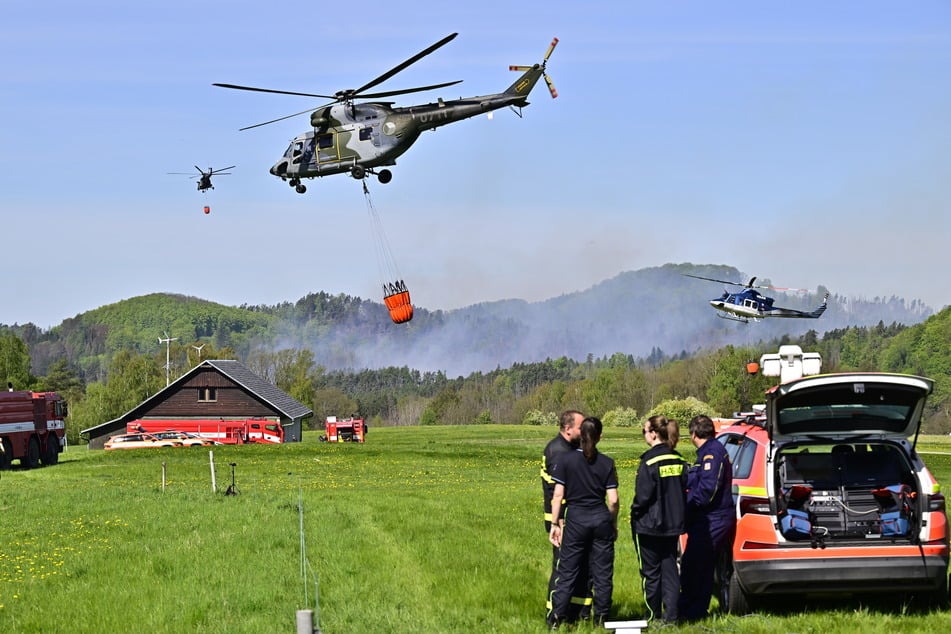Rund 500 Feuerwehrleute kämpfen im unwegsamen Gelände, Hubschrauber werfen Wasser ab.