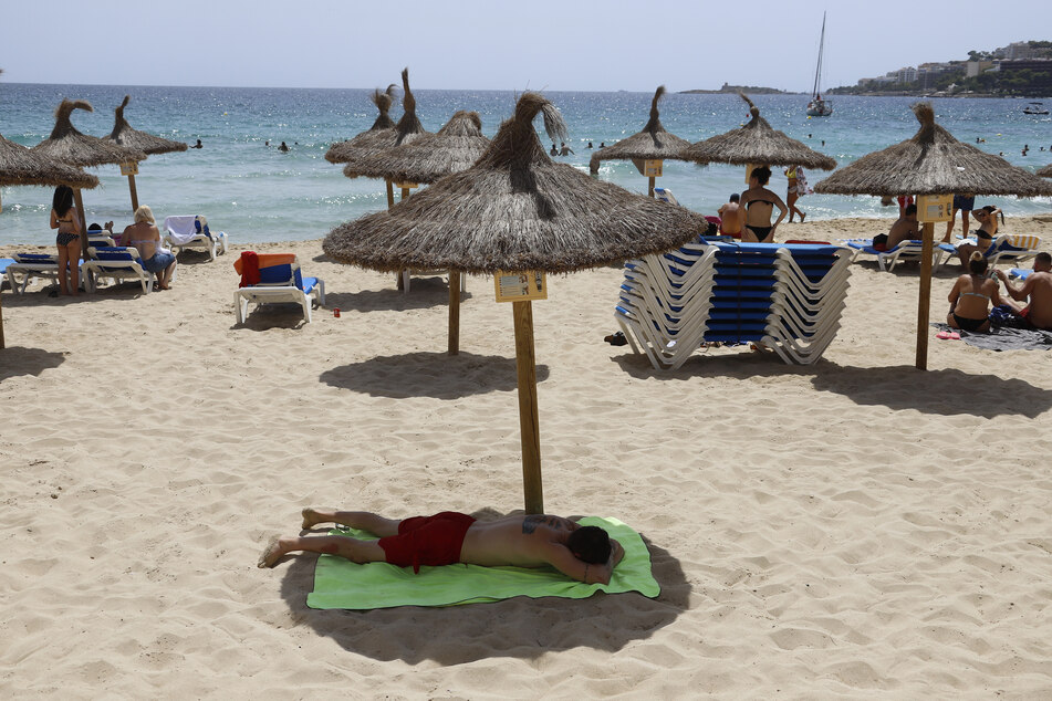 Ein Mann liegt unter einem Sonnenschirm am Strand von Cala Major. Mallorca und der Rest Spaniens gilt nun als Risikogebiet für deutsche Urlauber.