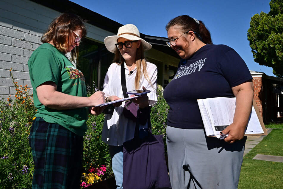 Volunteer canvassers Liz Grumbach (c.) and Patricia Jones (r.) meet Lucy Meyer (l.) who signs a petition outside her home in Phoenix, Arizona on Saturday as the volunteers go door-to-door for signatures to get the petition for the Arizona Abortion Access Act onto the November 2024 ballot for voters to decide.