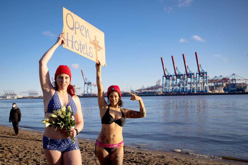 Eve Champagne (l), Burlesque-Künstlerin, und Natalie Warncke halten ein Schild, bevor sie mit anderen Menschen in die eiskalte Elbe springen.