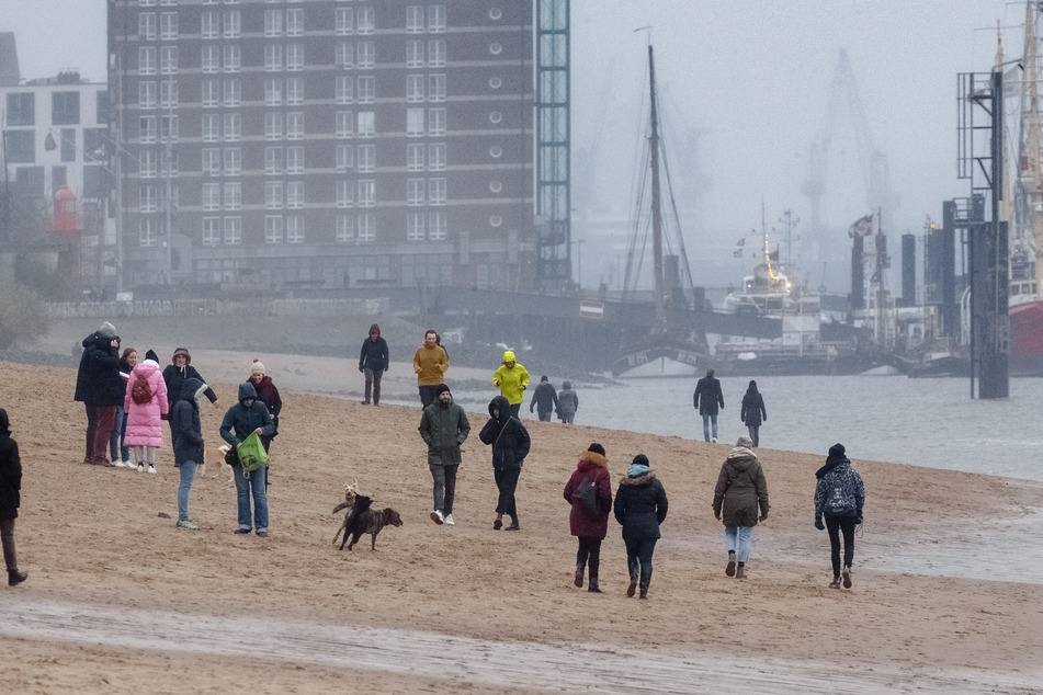 Spaziergänger sind bei Nieselregen am Elbstrand bei Övelgönne unterwegs.