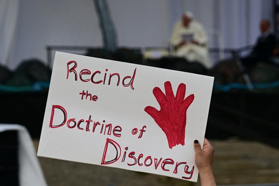 A person holds a protest sign reading "Recind the Doctrine of Discovery" as Pope Francis speaks on stage at Nakasuk Elementary School Square in Iqaluit, Nunavut, Canada.