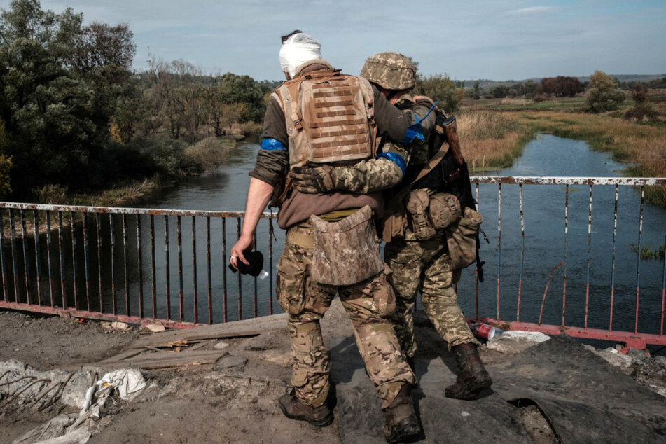 Ein ukrainischer Soldat hilft seinem verletzten Kameraden bei der Überquerung einer Brücke.