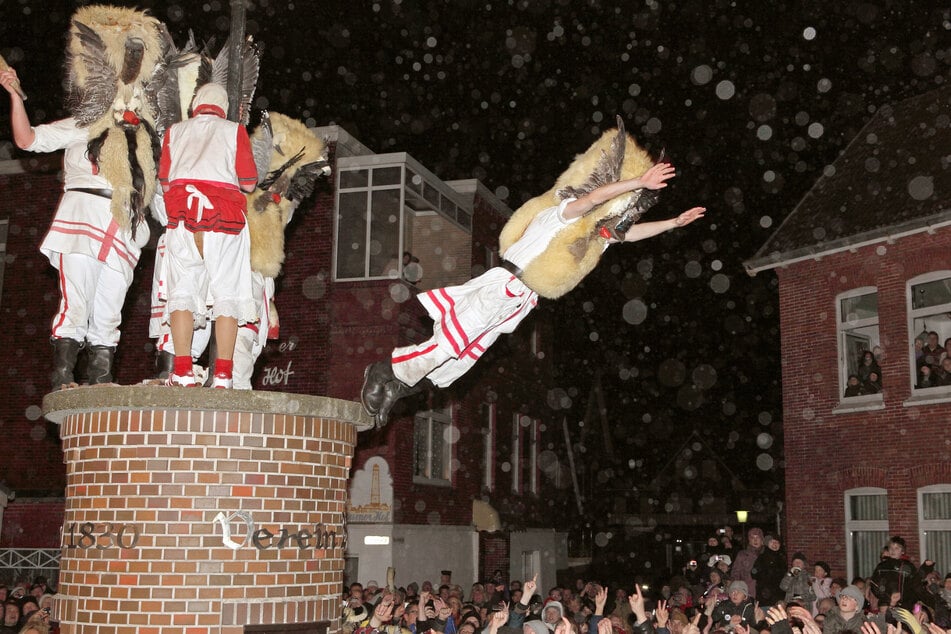 Mit Masken verkleidete Männer des Vereins Borkumer Jungens stürzen sich am Abend in der Innenstadt der Nordseeinsel von einer Litfaßsäule in die Arme der Schaulustigen. (Archivfoto)