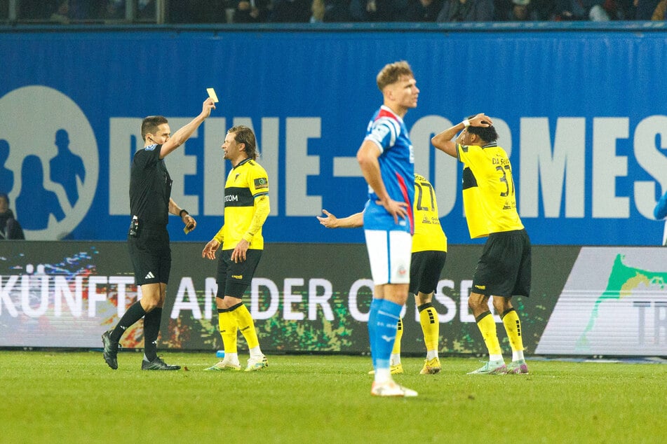 Joel da Silva Kiala (21, r.) sah nach seinem vermeintlichen Handspiel, das zum Elfmeter führte, auch noch Gelb, Kapitän Bentley Bahn (33, 2.v.l.) konnte es nicht fassen.