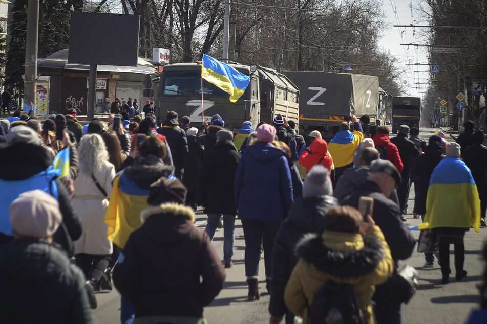 Menschen in Cherson tragen ukrainische Fahnen und gehen während einer Kundgebung gegen die russische Besatzung auf Lastwagen der russischen Armee zu.