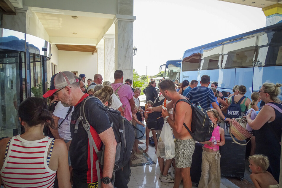 Touristen warten vor ihrem Hotel auf Rhodos auf den Einstieg in Busse, um die Insel zu verlassen.