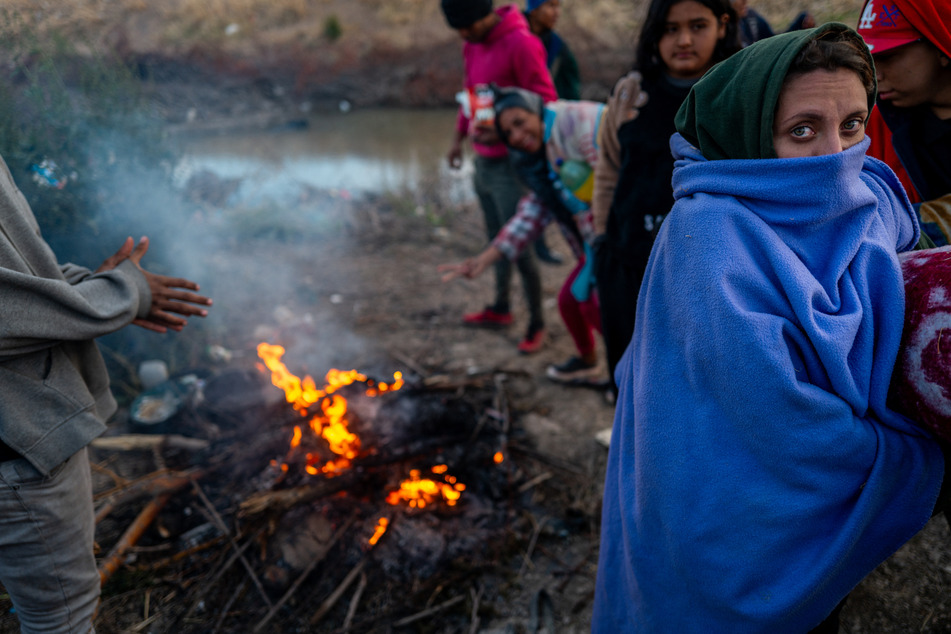 Migrant Palanqa Guaremala (r.), keeps warm by a fire on the US side of the Rio Grande river on March 26, 2024 in El Paso, Texas.
