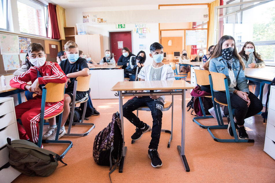 Schüler einer 7. Klasse sitzen zu Beginn des Unterrichts mit Mund-Nasen-Bedeckungen im Klassenraum.