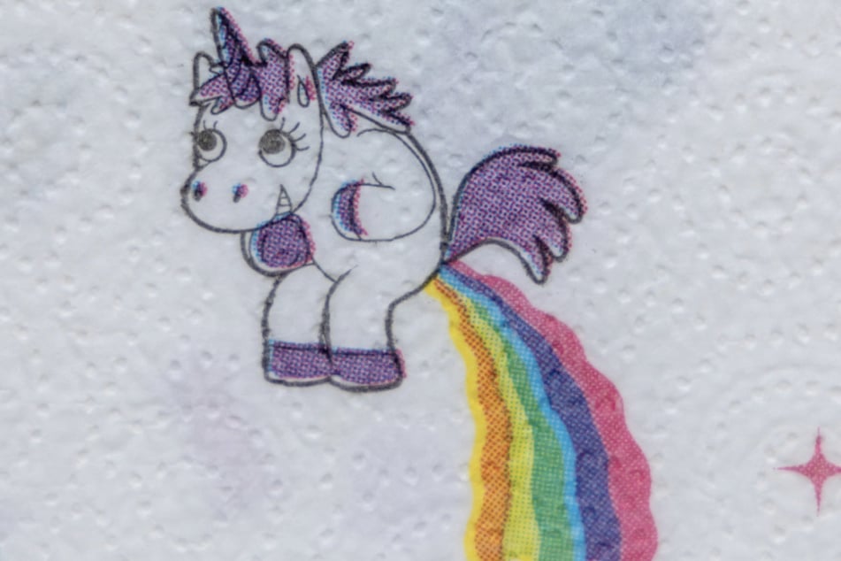 Farbige Flatulenz: Auf einem Papierstreifen grinst ein Einhorn, das einen Regenbogen auspupst.