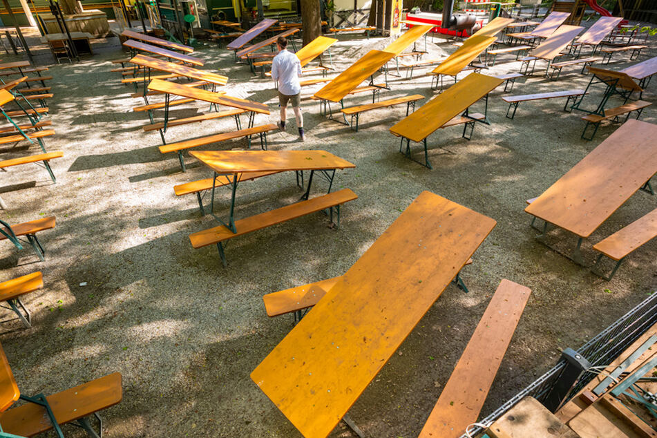 Ein Gasthausmitarbeiter geht zwischen zusammengestellten Biertischen entlang, die im geschlossenen Seehaus-Biergarten in München stehen.