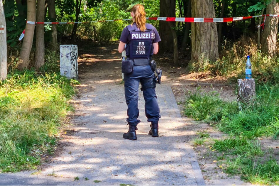 Eine Polizistin steht vor einem Flatterband in dem Wald bei Potsdam.